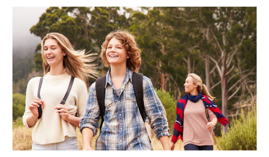 Twee jonge meiden en een vrouw wandelen in de bossen. Ze hebben een vrolijke lach op hun gezicht.